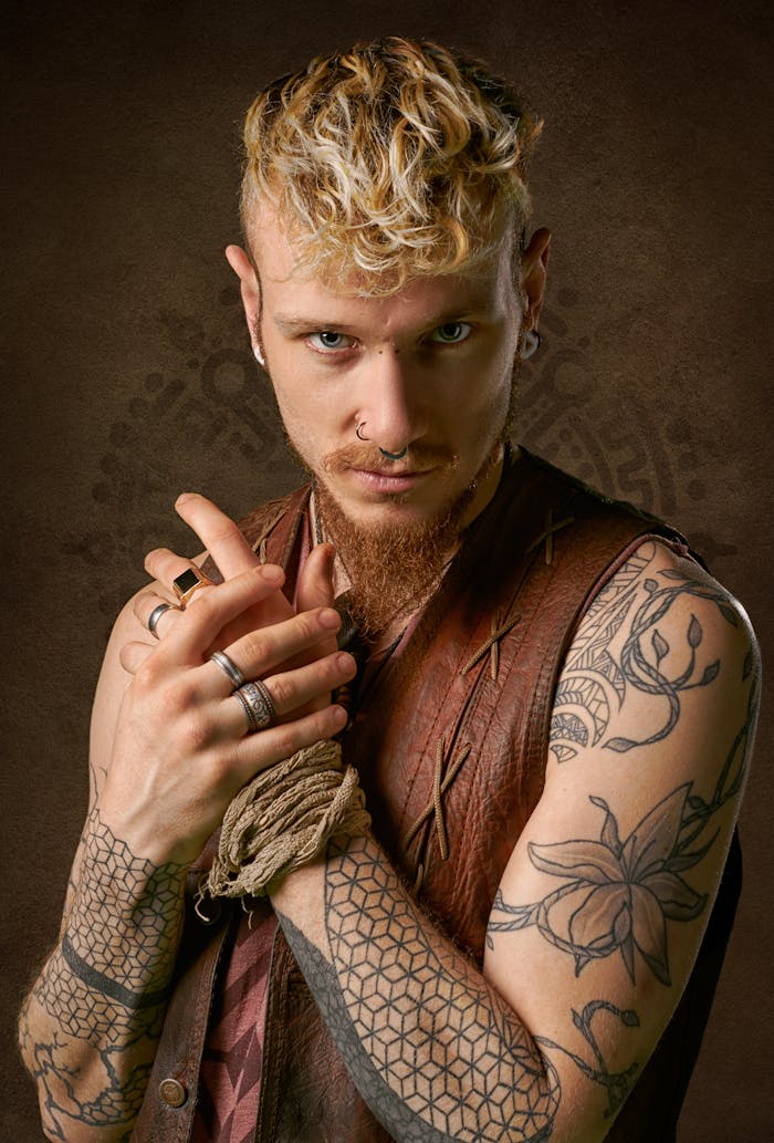 Close-up portrait of a stylish young man with tattoos, blond hair, and a punk aesthetic indoors.