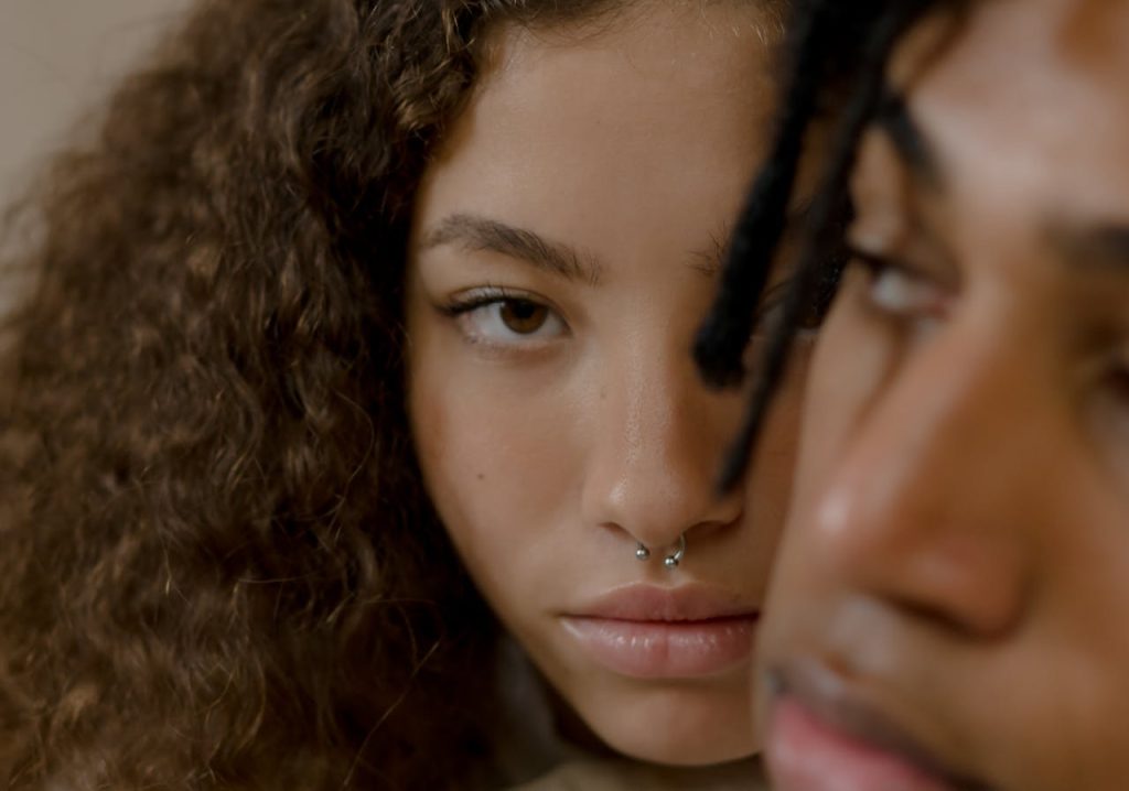 Intimate close-up of a young couple highlighting their facial piercings and curly hair.