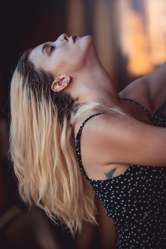 Profile of a tattooed woman looking up, emphasizing her piercings. Captured in a warm, moody tone.